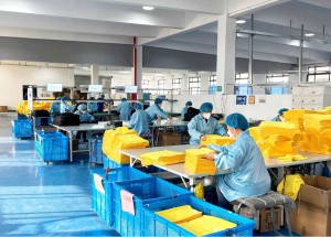 Workers in blue protective clothing handling yellow fabrics in a factory