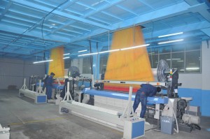 Workers operating textile machinery in a factory with yellow threads
